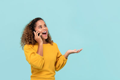 Smiling young woman using smart phone against gray background