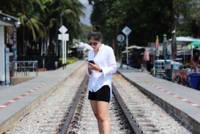 Young woman using phone while standing on railroad track