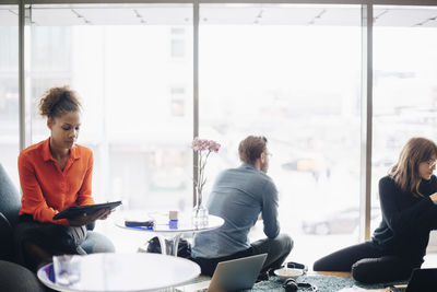 Multi-ethnic business colleagues sitting against window in cafeteria at office