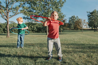 Full length of boys playing with plastic hoops on grassy land in park