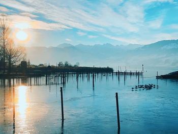 Wooden posts in lake against sky during sunset