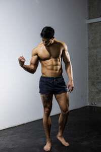 Full length of shirtless man standing against wall