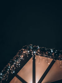 Low angle view of illuminated lighting equipment against black background