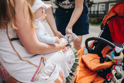 Man assisting baby in wearing shoes held by mother