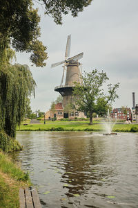 Traditional windmill by river against sky