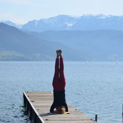 Woman exercising on pier over lake against mountains