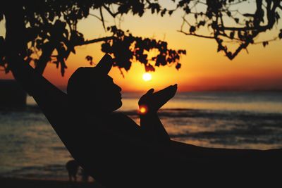 Silhouette hand against sea during sunset