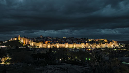 Illuminated city against cloudy sky at night