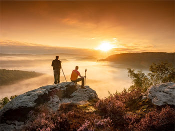 Two hotographers on hilltop at tripod camera search object of composition  at sunset. man take photo