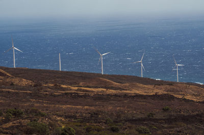 Windmill on field by sea against sky