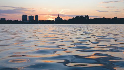 Scenic view of lake by buildings against sky during sunset