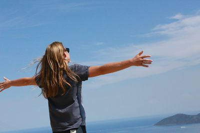 Rear view of woman with arms outstretched by sea against sky