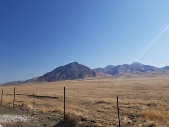 Scenic view of field by mountains against clear blue sky