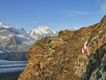 Scenic view of snowcapped mountains by exposed hiking trail against blue sky