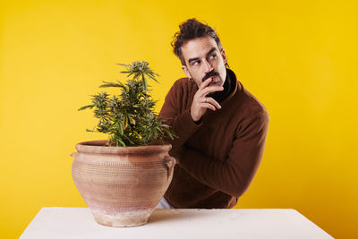 Portrait of young woman holding potted plant against yellow background