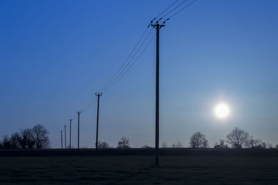 Electricity pylons on field against clear sky