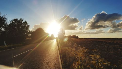 Road amidst field against sky during sunset