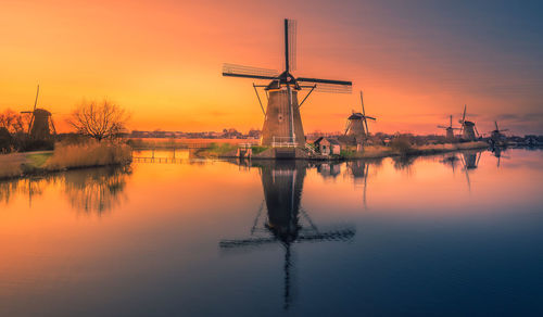 Traditional windmill by lake against sky during sunset