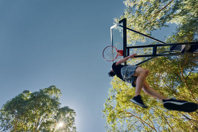 Low angle view of man putting ball in basketball hoop against clear sky