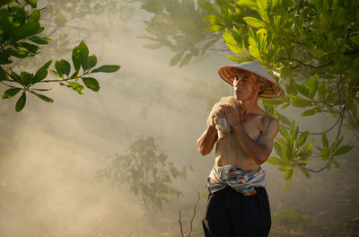 Shirtless senior man holding fishing net at forest