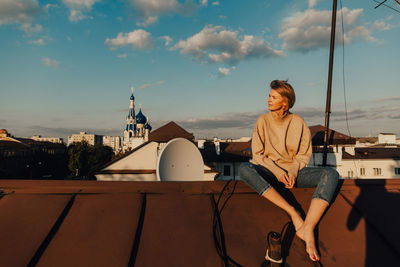 Woman sitting on rooftop against sky