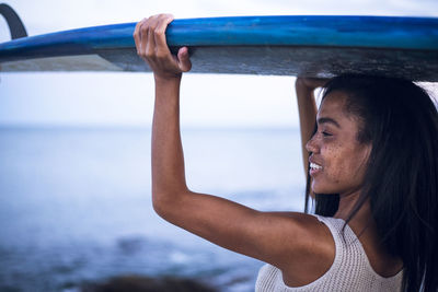 Black multiracial woman lifestyle portrait by the ocean with surfboard