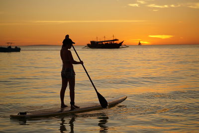 Silhouette person in sea against sky during sunset