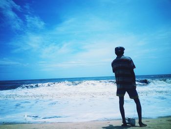 Rear view of man standing on beach against blue sky