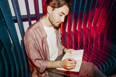 Young male entrepreneur writing in diary while sitting on seat at office