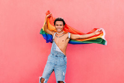 Portrait of gay man holding rainbow flag against pink background