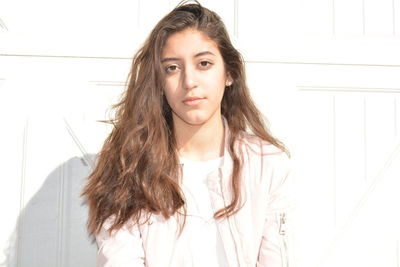 Close-up portrait of young woman standing by wall on sunny day