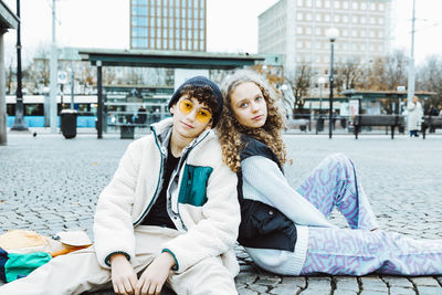 Portrait of male and female friends sitting on footpath in city