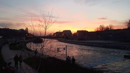 Reflection of silhouette trees on wet shore against sky during sunset