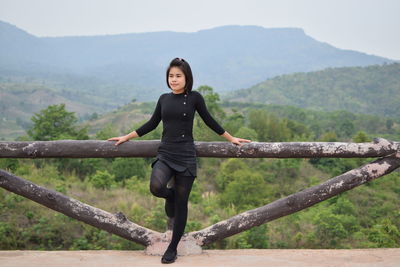 Young woman looking away while standing by railing on observation point against mountain