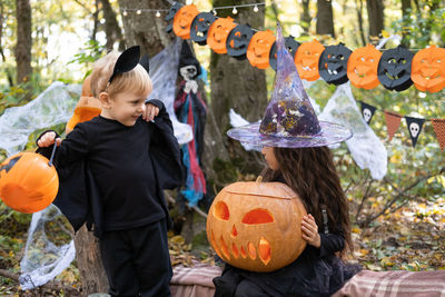 Two kids girl and boy in halloween costume with pumpkins in halloween decorations outdoor