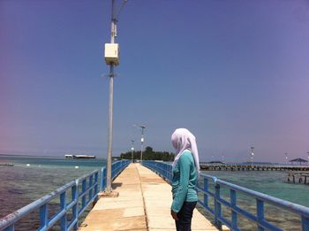 Rear view of woman standing on pier over sea against clear sky