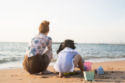 Rear view of woman sitting on beach against sky