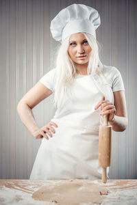 Portrait of young woman holding rolling pin while standing in kitchen