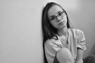 Portrait of young woman sitting against wall