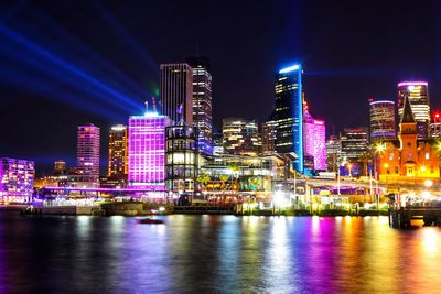 Illuminated buildings by river against sky in city at night