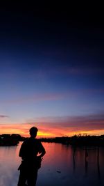 Silhouette man standing by lake against sky during sunset
