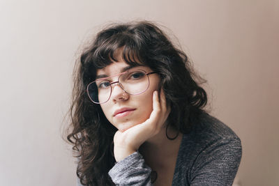 Portrait of beautiful young woman with hand on chin sitting against wall