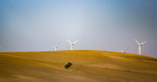 Wind turbines on field against clear sky