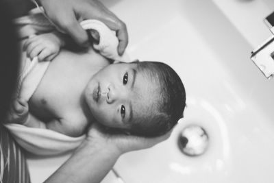 Cropped hands of parent holding newborn son at sink