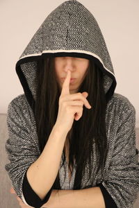 Woman wearing hood with finger on lips at home