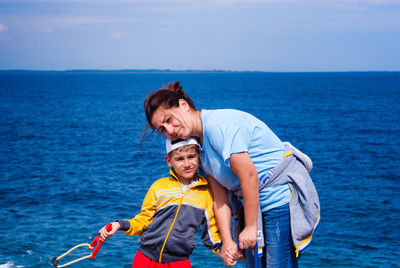 Portrait of woman standing with son by sea against sky