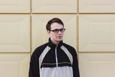 Smiling young man wearing eyeglasses while standing against wall