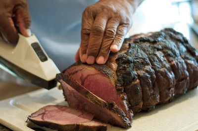 Cropped image of hand cutting meat with knife on cutting board