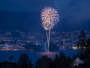 Firework display over illuminated city against sky at night