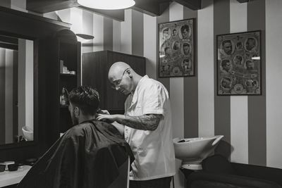 Side view of barber cutting man hair in salon